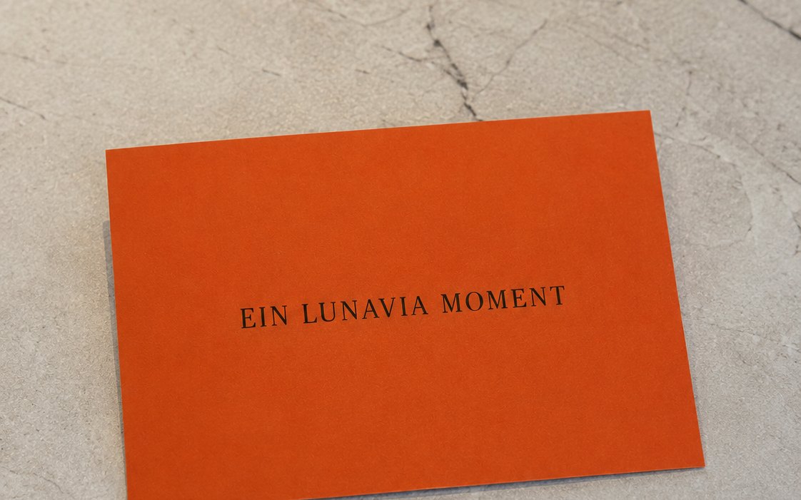 LunaVia Gutschein – orange Karte mit der Aufschrift „Ein LunaVia Moment“ auf Marmor